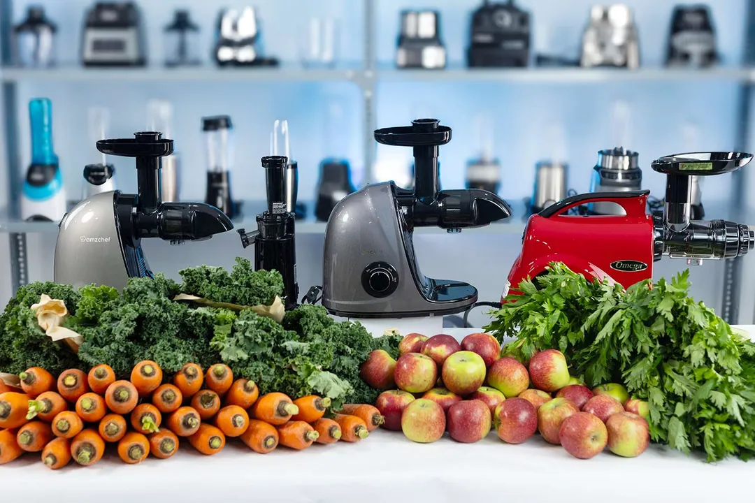 Piles of carrots, apples, kale, and celery in front of several masticators in test to find the best masticating juicers