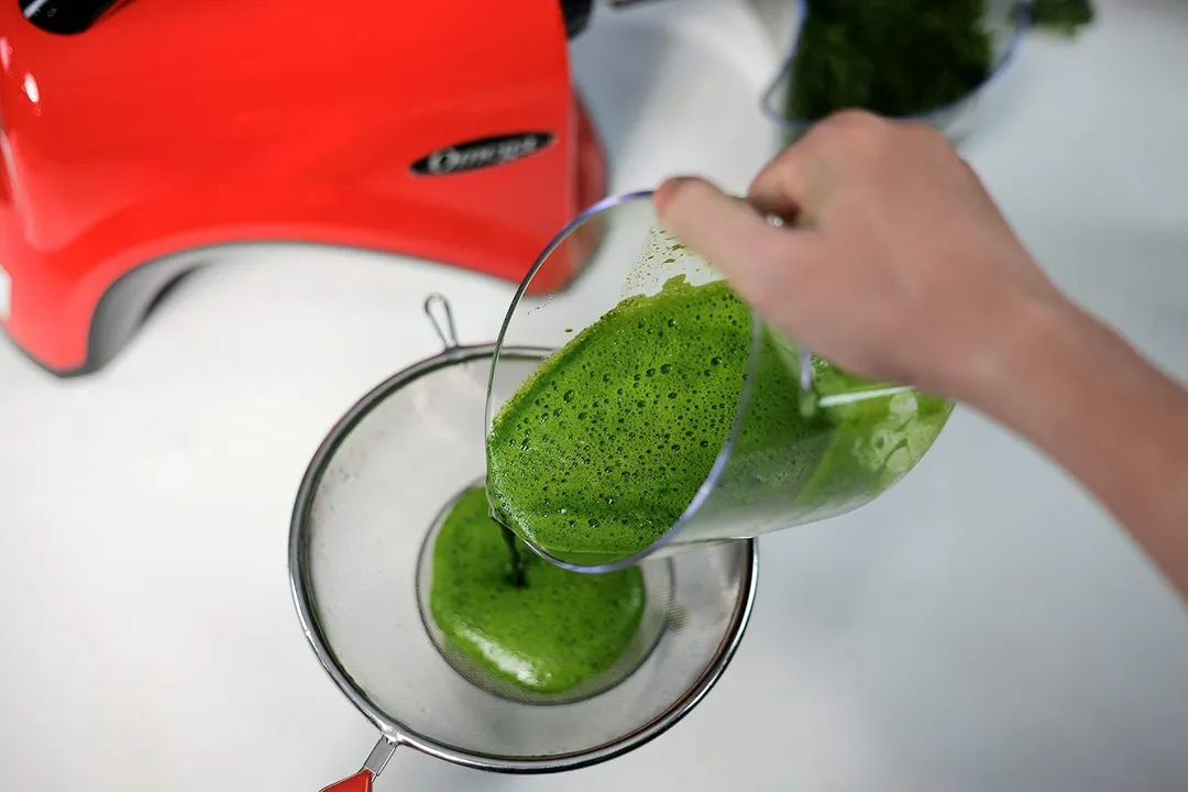 Foamy green juice being strained using a spoon and strainer