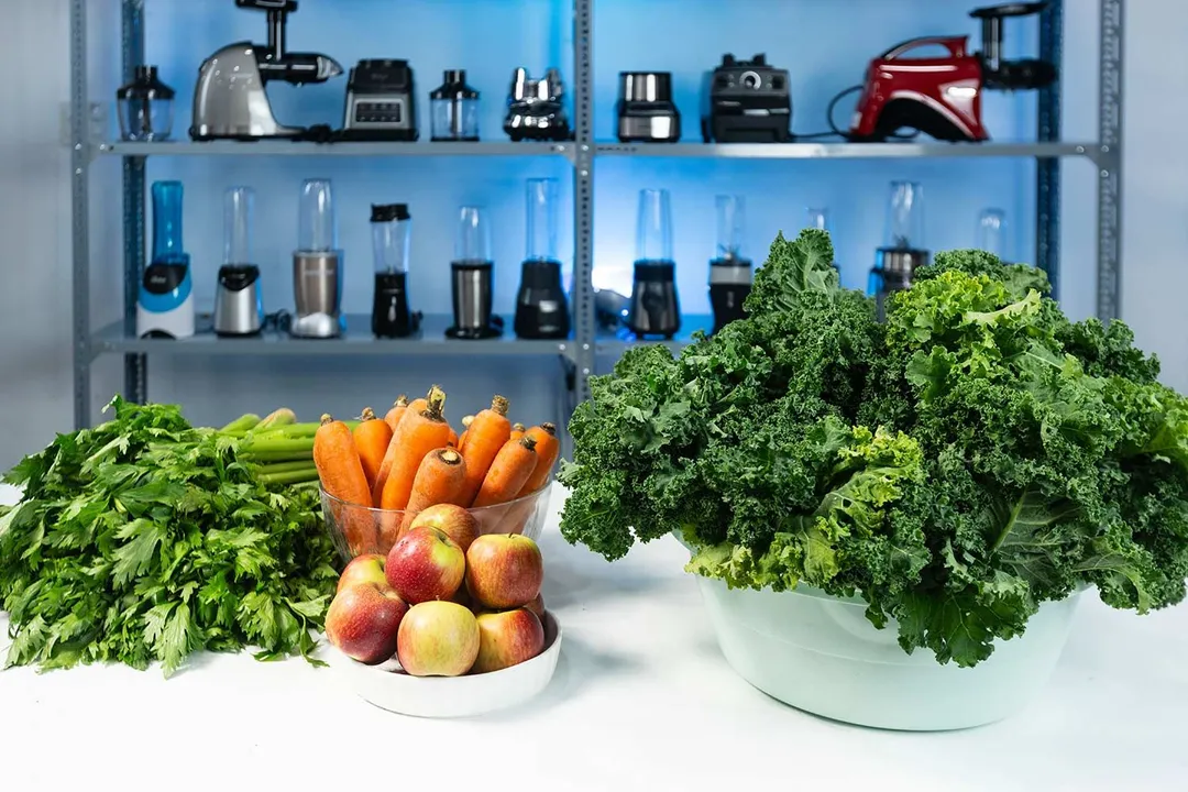 Piles of carrots, kale, apples, and celery with different masticating juicers