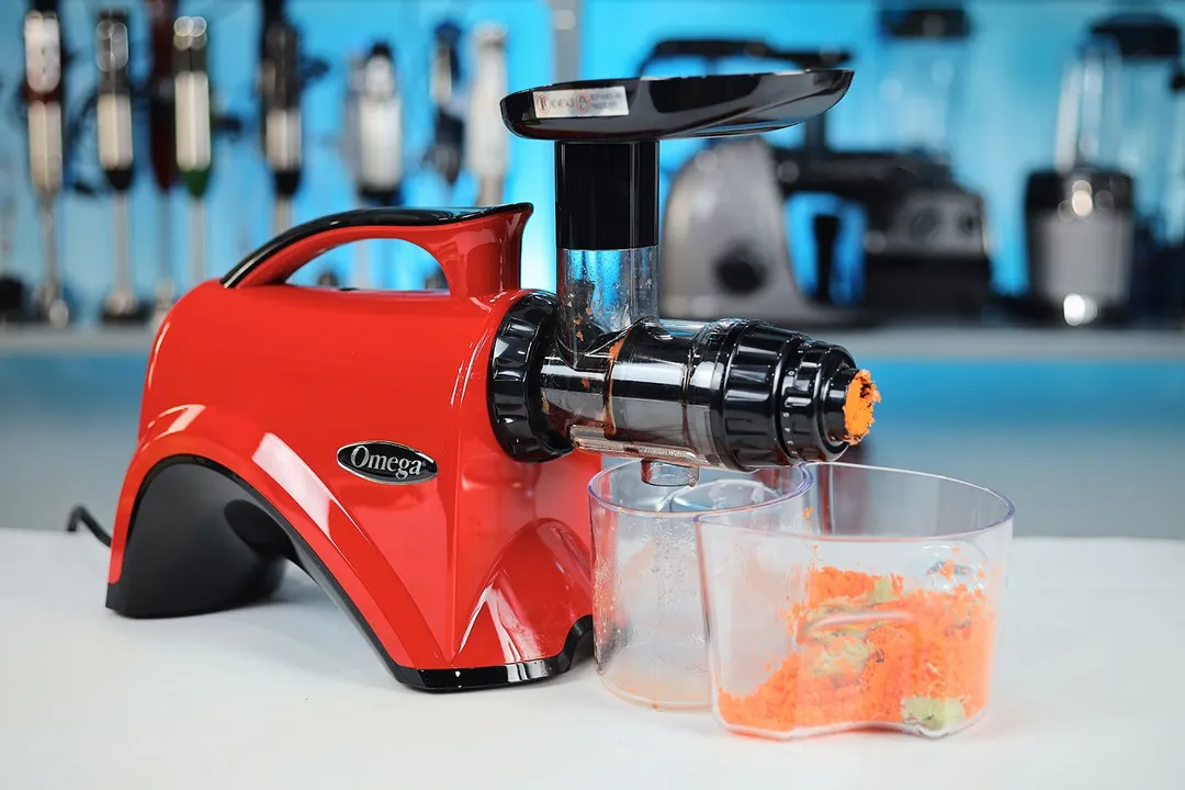 The red Omega NC900 masticating juicer, fully assembled, with carrot pulp in the pulp collector