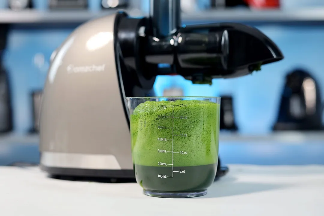 Cup of kale juice in front of a masticating juicer