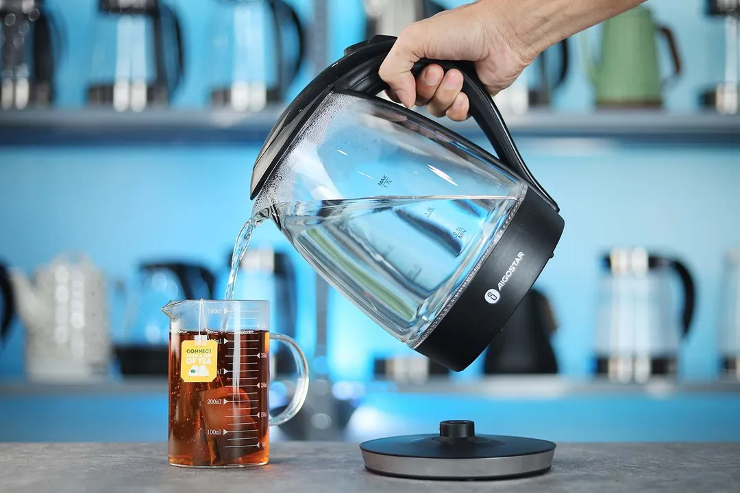 A hand pouring water from the Aigostar Electric Kettle 300104LCB into a glass of black tea.