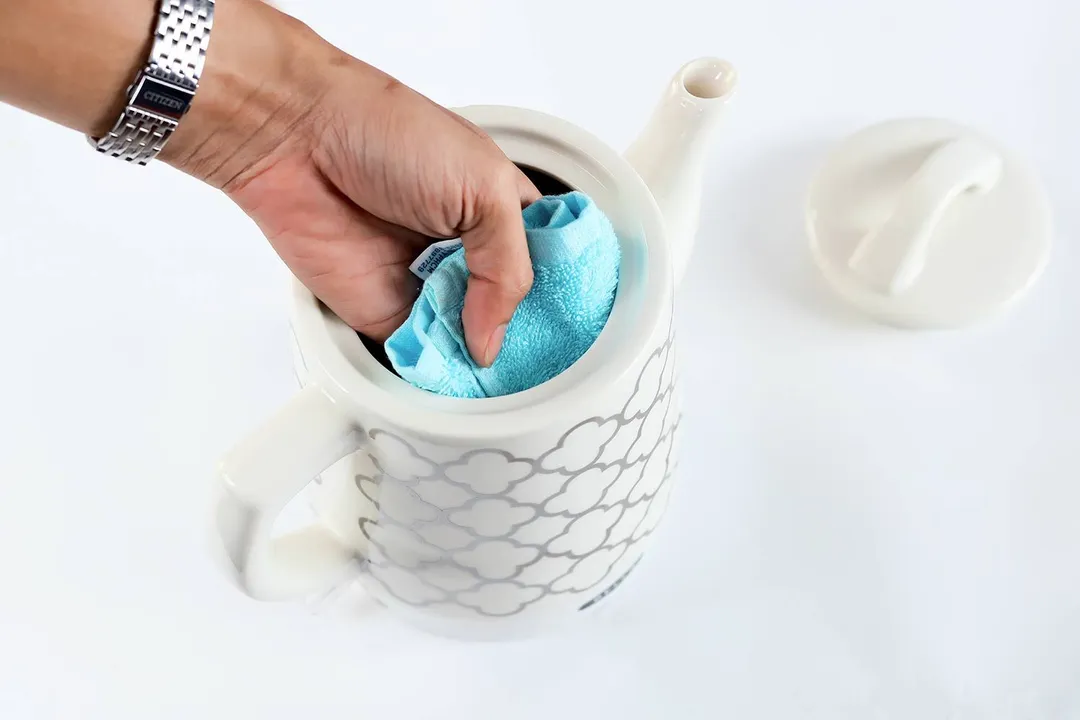 A hand holding a blue cloth wiping the interior of the Bella Ceramic Gooseneck Electric Kettle (14745).