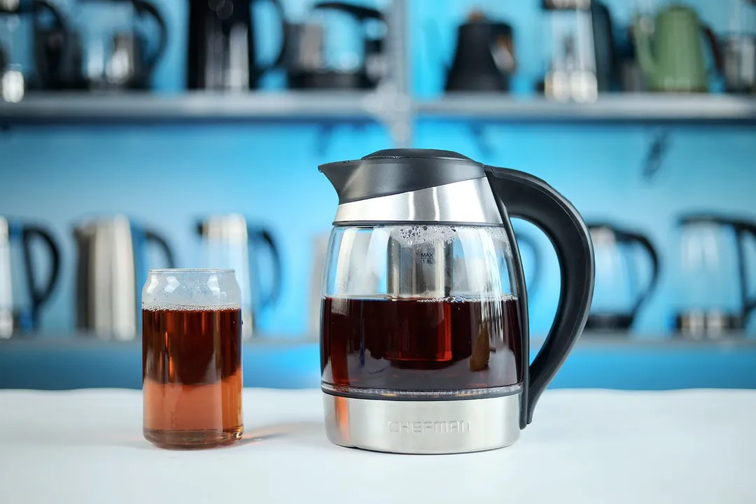 On the right, the Chefman Electric Kettle with 5 Presets (RJ11-17-CTI-RL) has a tea infuser for direct brewing. On the left is a glass of black tea.