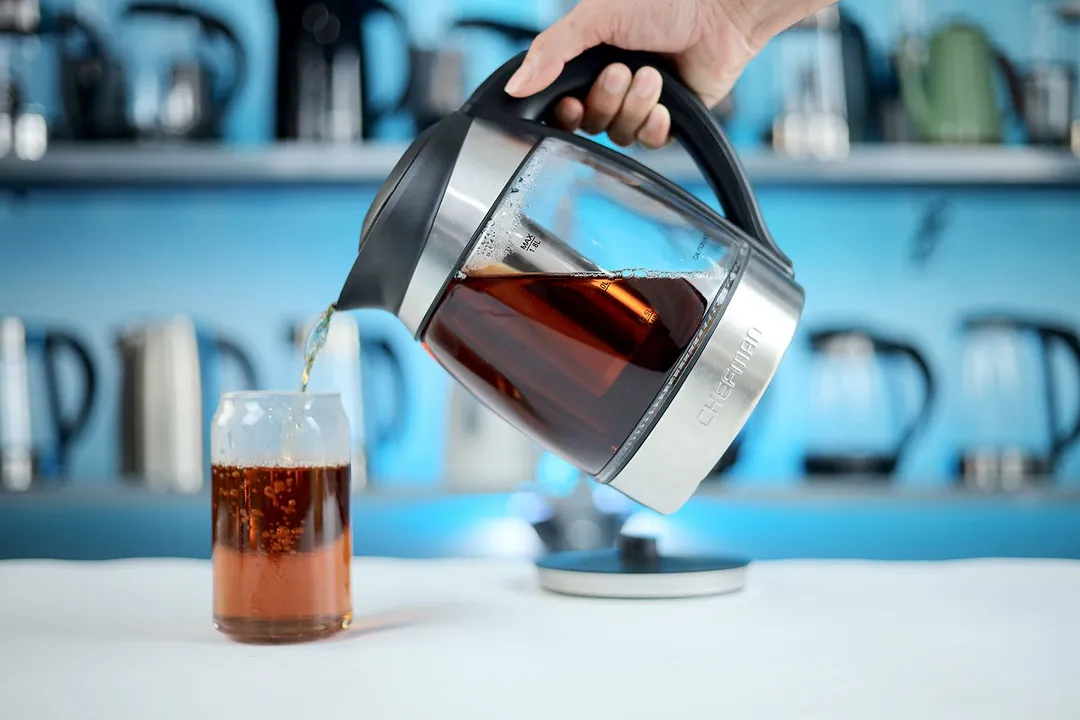 A hand pouring tea from the Chefman Electric Kettle with 5 Presets (RJ11-17-CTI-RL) into a glass.