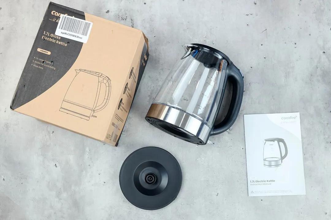 On the upper left is the Comfee Glass Electric Kettle (CEKG003). On the right is a cardboard box. Below the kettle, on the right is an instruction manual and on the left is the power base.