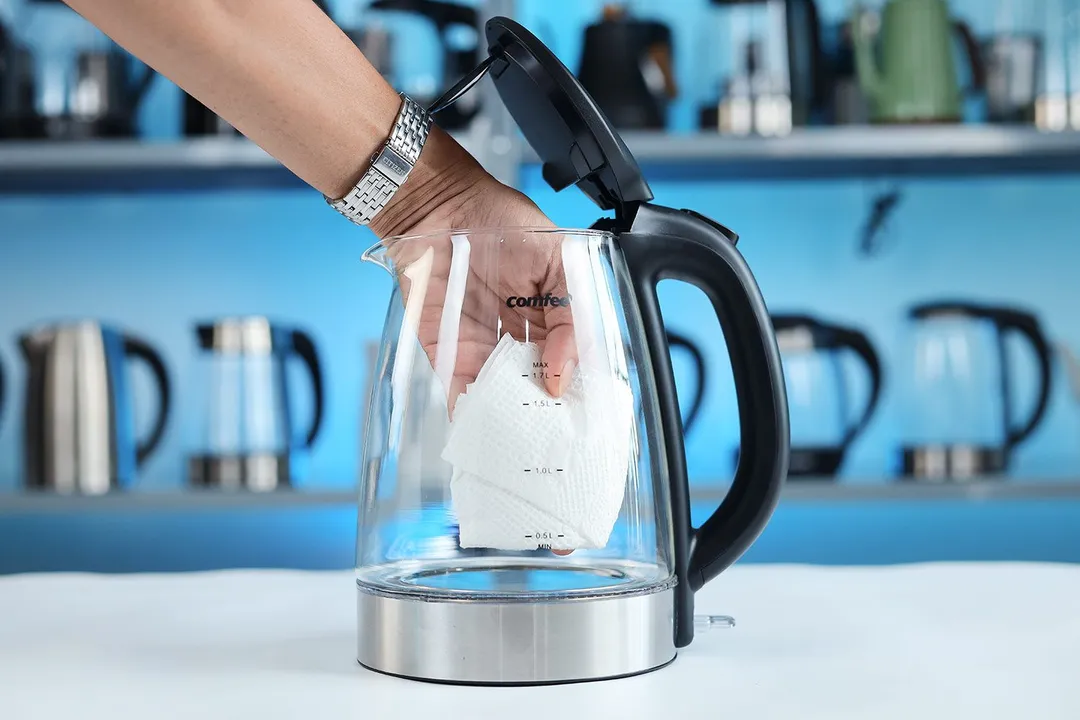 A  hand wiping the carafe interior of the Comfee Glass Electric Kettle (CEKG003) with a piece of tissue.