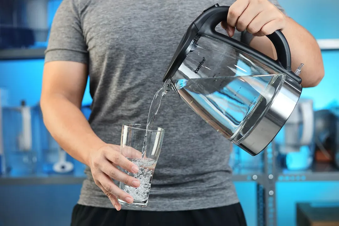 A person in a grey shirt pouring water from the Comfee Glass Electric Kettle (CEKG003) into a glass.