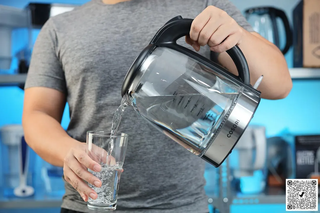 A person in a grey shirt pouring water from the Cosori Glass Electric Kettle (GK172-CO) into a glass.