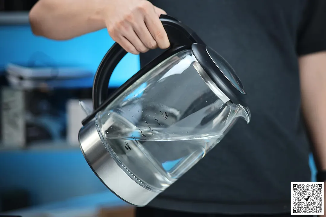 A hand holding the Cosori Glass Electric Kettle (GK172-CO)  by its handle.