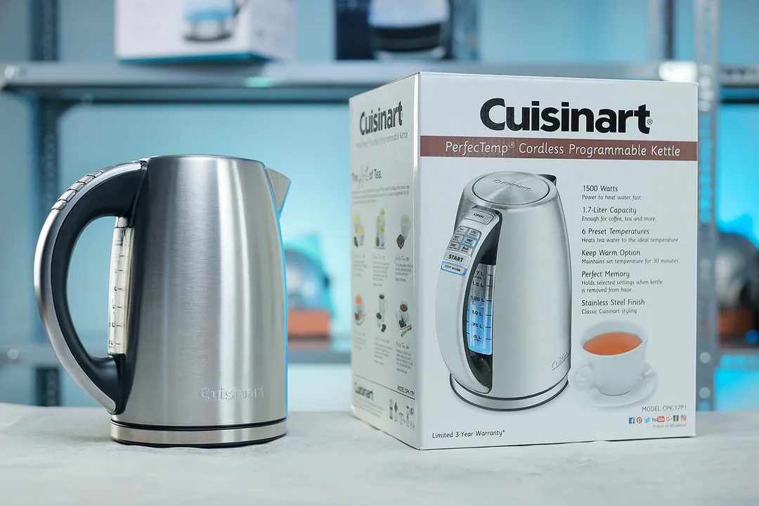 The Cuisinart Stainless Steel Electric Kettle with 6 Preset Temperatures (CPK-17P1 PerfecTemp) to the left and its cardboard box on the right. In the background is a shelf with various electric kettles.