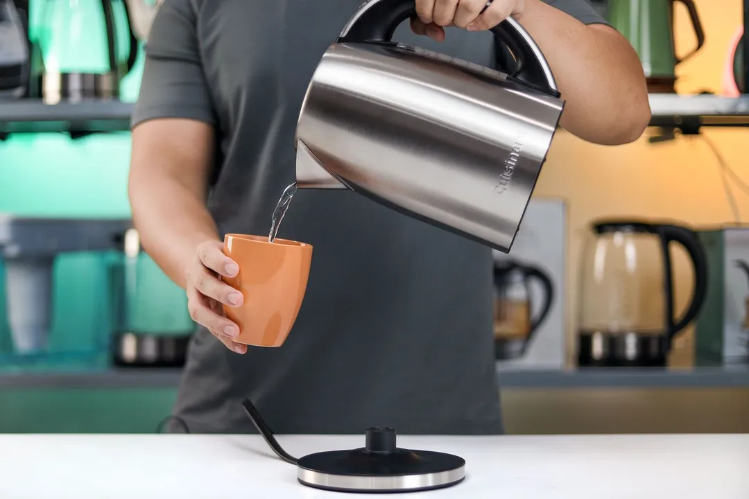 A person in a grey shirt pouring water from the Cuisinart Stainless Steel Electric Kettle with 6 Preset Temperatures (CPK-17P1 PerfecTemp) into a cup.
