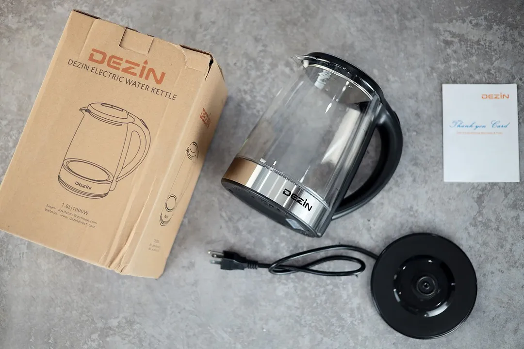 On the upper right is the Dezin Electric Glass Kettle DZ380. On the left is a cardboard box. Below the kettle, on the right is an instruction manual and on the left is the power base.