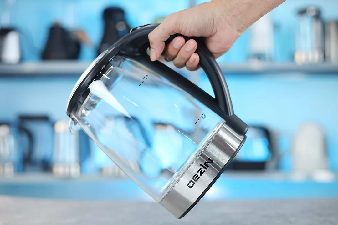 A hand holding the Dezin Electric Glass Kettle DZ380 by its handle.