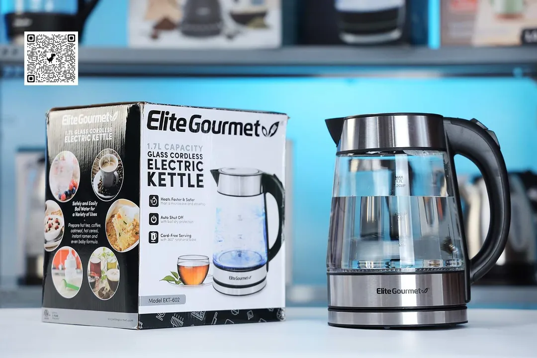 The Elite Gourmet Electric Kettle (EKT-602) on the right and its cardboard box on the left. In the background is a shelf with different electric kettles.