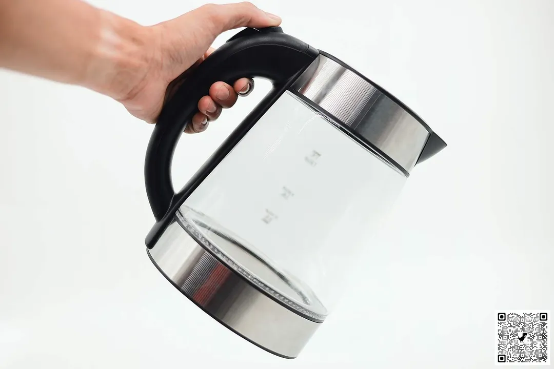 A hand holding the Elite Gourmet Electric Glass Kettle (EKT-602) by its handle.