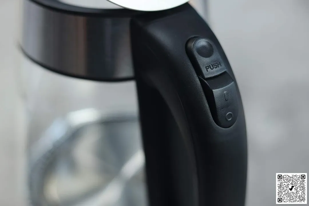 The handle of the Elite Gourmet Electric Glass Kettle (EKT-602) has two buttons, the one above is the lid button and below is the power switch.