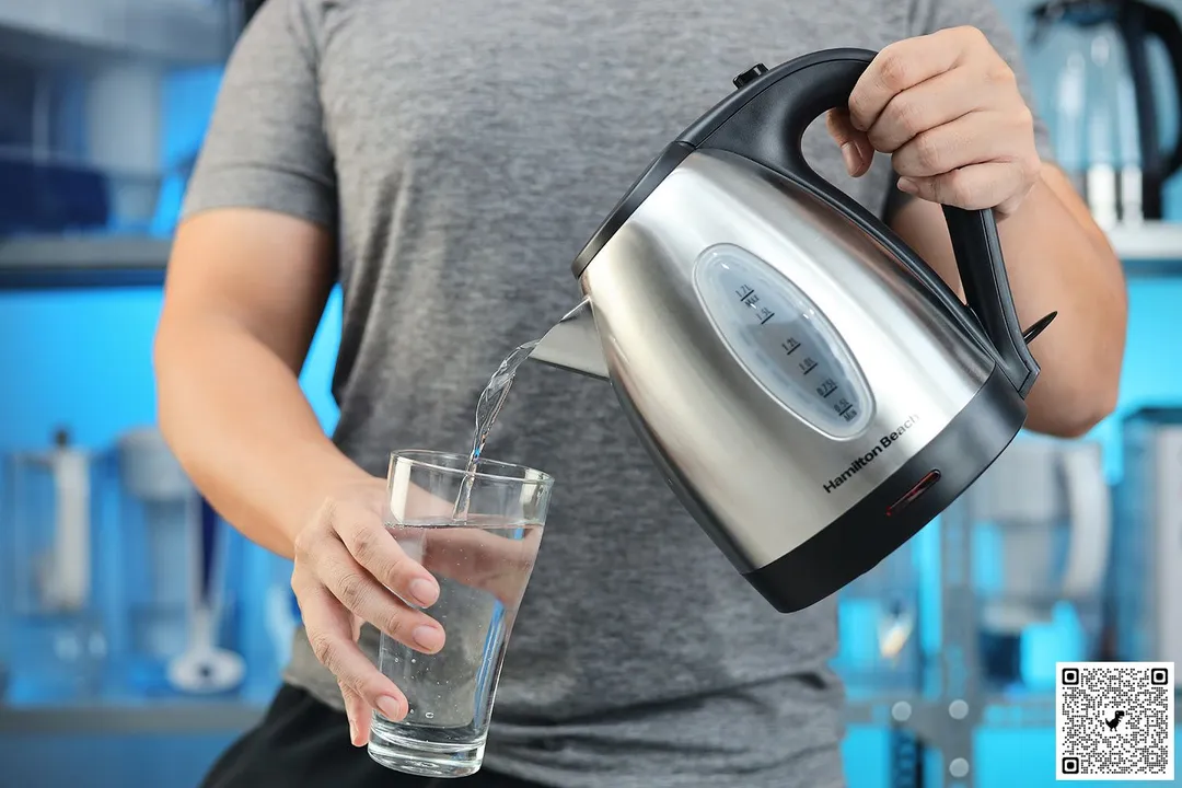A person in a grey shirt pouring water from the Hamilton Beach Stainless Steel Electric Kettle (40880) into a glass.