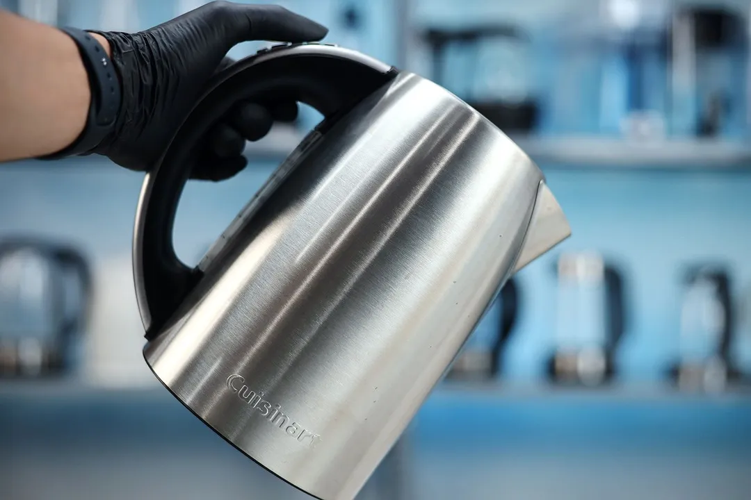 A hand holding the Cuisinart Stainless Steel Electric Kettle with 6 Preset Temperatures (CPK-17P1 PerfecTemp) by its handle.