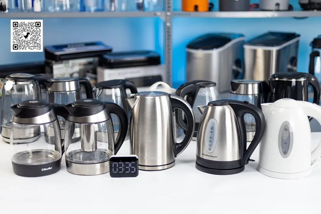 On a white table is 12 electric kettles. In front of them is a dark-screen digital timer displaying 3 minutes 35 seconds. In the background is a shelf of ice-makers.