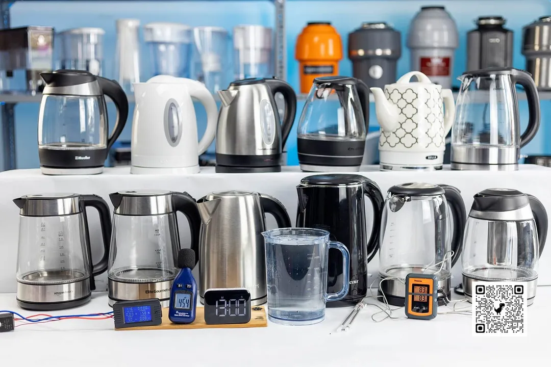 In the front, from left to right is a grey power meter, a blue noise meter, a dark-screen digital timer, a measuring cup filled with water, and an orange two-probe ThermoPro digital thermometer. Behind them are two rows of electric kettles, 6 on each row.