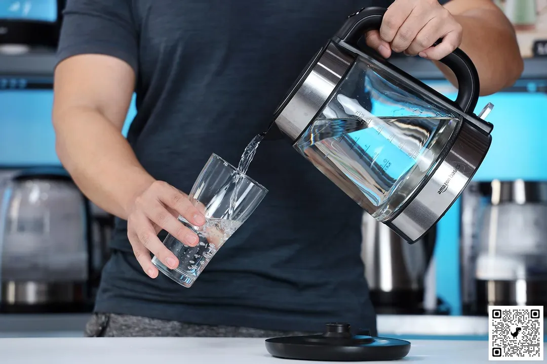 A person in a dark green shirt pouring water from the Amazon Basics Electric Glass and Steel Kettle F-625C into a glass.