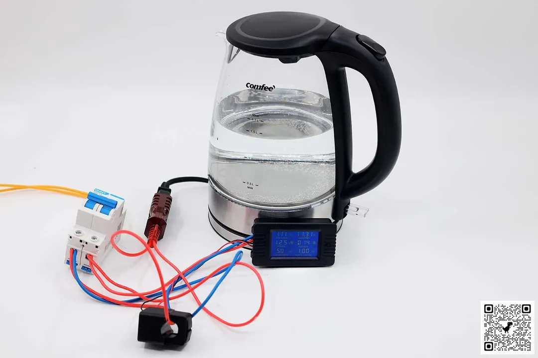 On a white table is a circuit breaker connected to a power meter, both of which are connected to the Comfee Glass Electric Kettle (CEKG001) using a plug adapter.