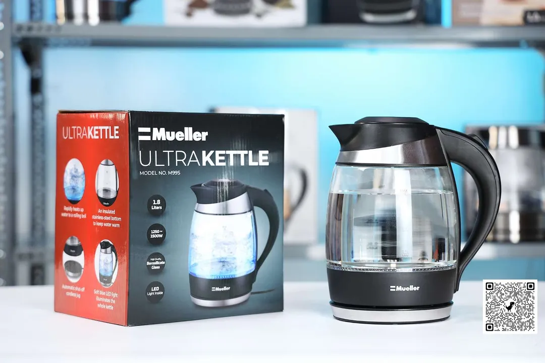 The Mueller Ultra Kettle (M99S) on the right and its cardboard box on the left. In the background is a shelf with different electric kettles.