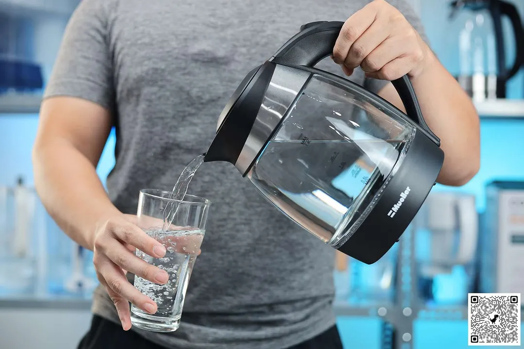 A person in a grey shirt pouring water from the Mueller Ultra Electric Kettle (M99S) into a glass.