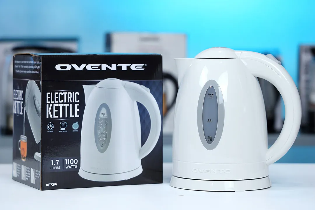 The Ovente Electric Kettle KP72W on the right and its cardboard box on the left. In the background is a shelf with different electric kettles.