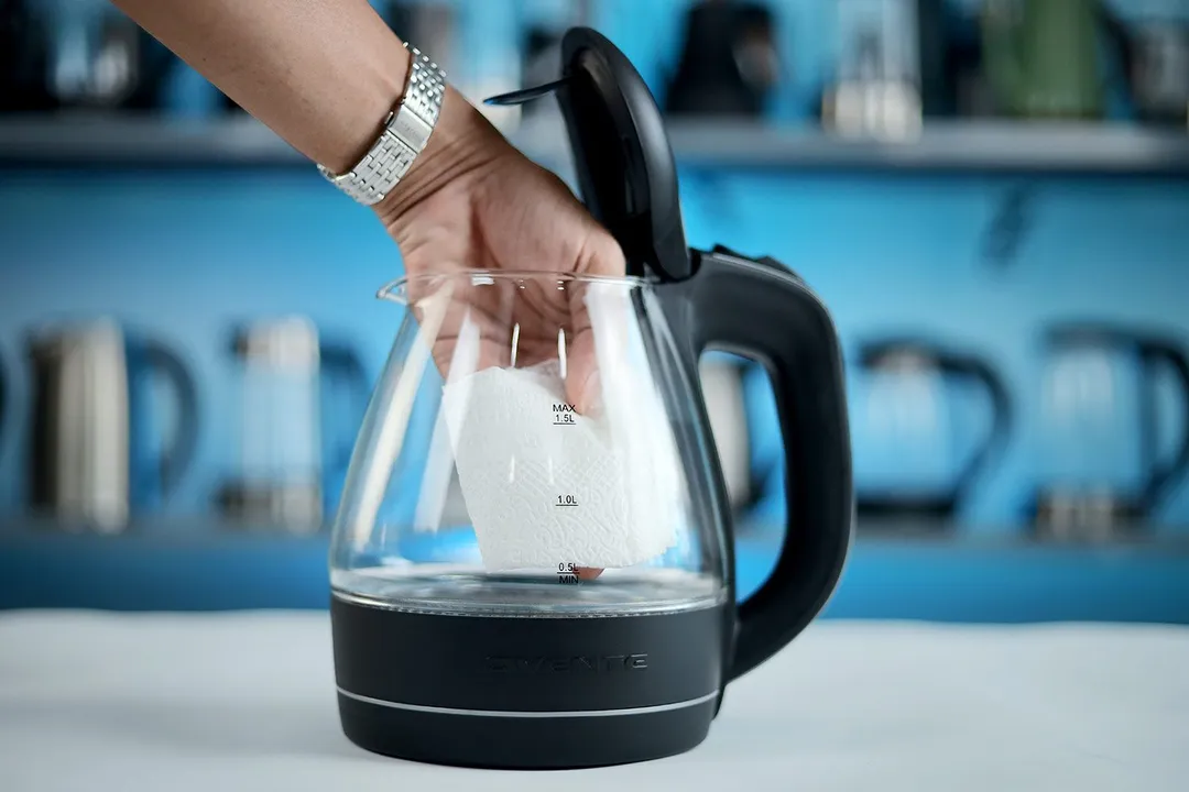 A  hand wiping the carafe interior of the Ovente Electric Glass Kettle (KG83B) with a piece of tissue.