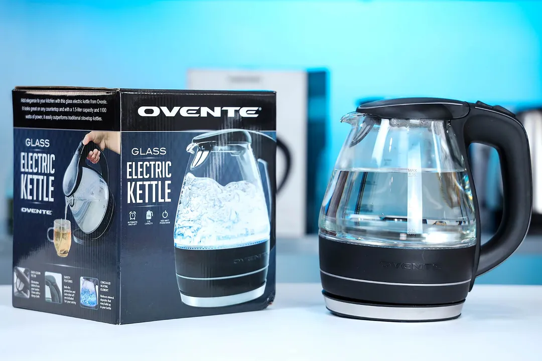 The Ovente Electric Glass Kettle (KG83B) on the right and its cardboard box on the left. In the background is a shelf with different electric kettles.