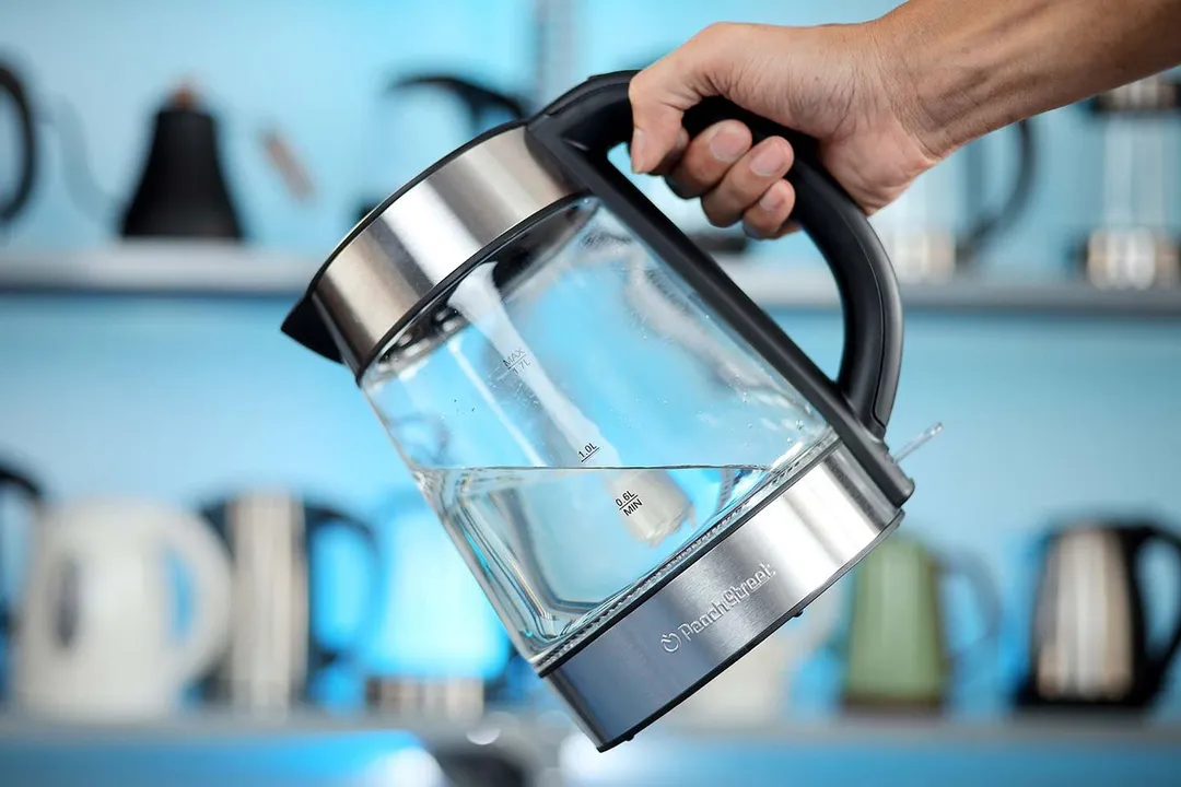 A hand holding the Peach Street Electric Kettle PE-1300 by its handle.