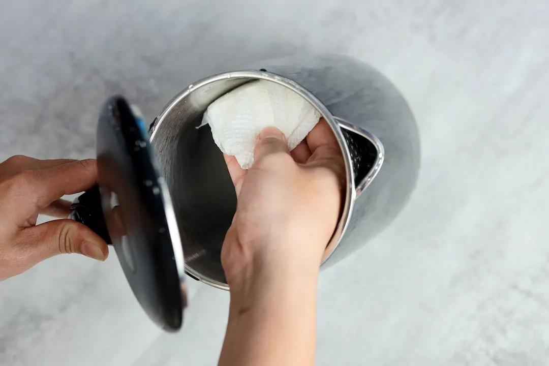 A hand holding a tissue wiping the interior of the Secura Electric Stainless Steel Double-Wall Kettle (SWK-1701DA).