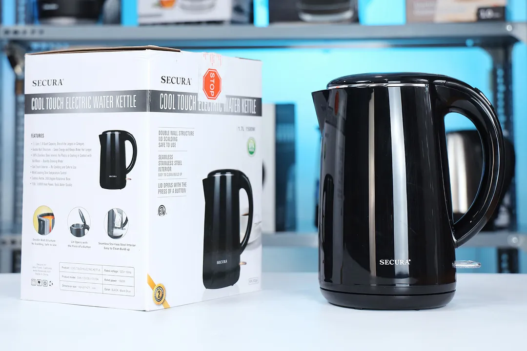 The Secura Electric Stainless Steel Double-Wall Kettle (SWK-1701DA) on the right and its cardboard box on the left. In the background is a shelf with various electric kettles.