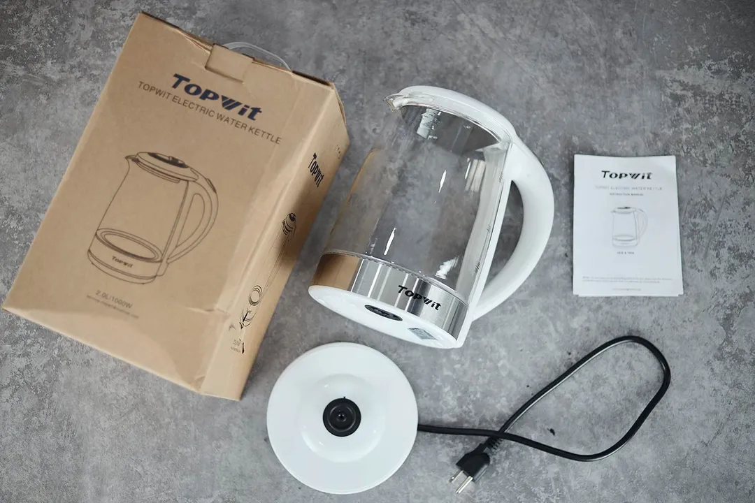 On the upper right is the Topwit Glass Electric Tea Kettle T630. On the left is a cardboard box. Below the kettle, on the right is an instruction manual and on the left is the power base.