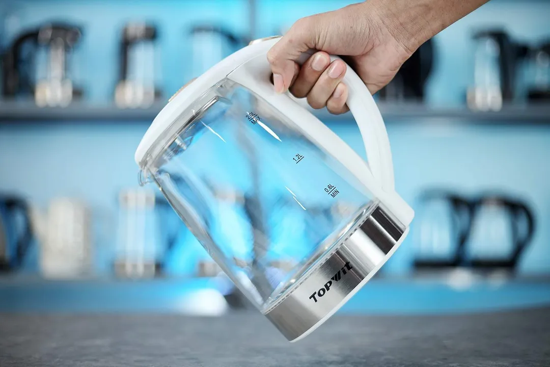 A hand holding the Topwit Glass Electric Tea Kettle T630 by its handle.