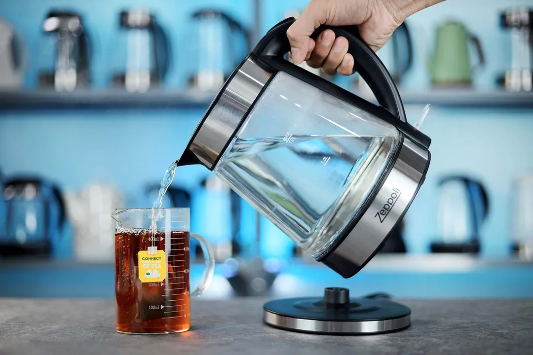 A hand pouring water from the Zeppoli Electric Kettle ZPL-KETTLE into a glass of black tea.