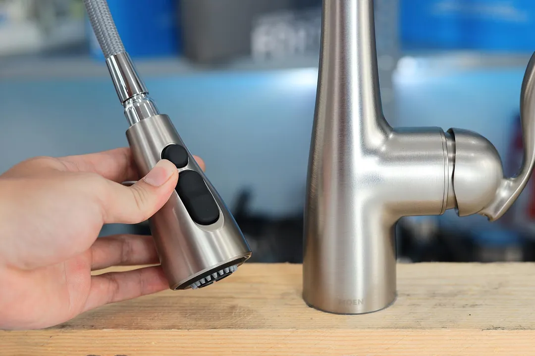 Hand holds a sprayer head of the Moen Arbor 7594 kitchen faucet and presses on the function button.