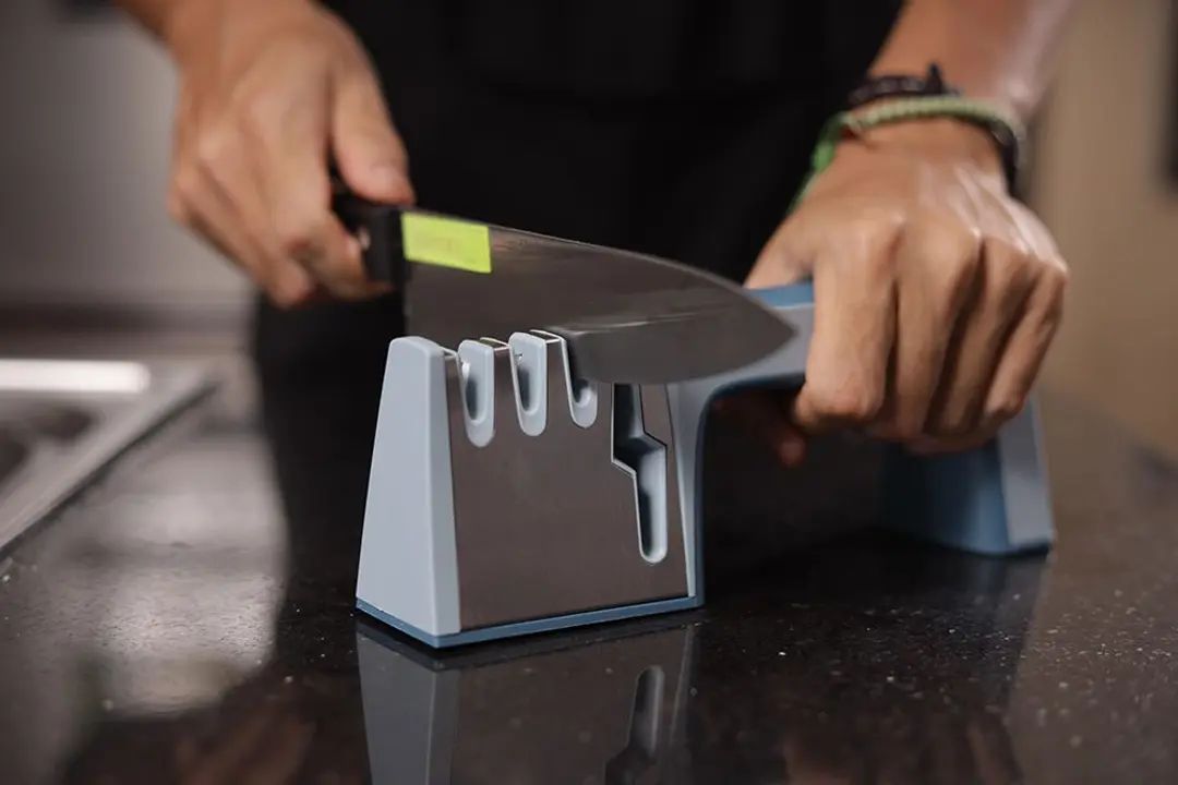 2 hands holding and sharpening a kitchen knife with the Wamery sharpener on a countertop