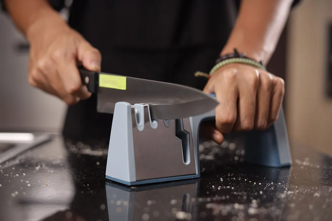 2 hands holding and sharpening a kitchen knife with the Wamery on a salt-sprinkled countertop
