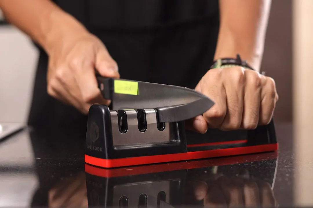 2 hands holding and sharpening a kitchen knife with the Cubikook sharpener on a countertop