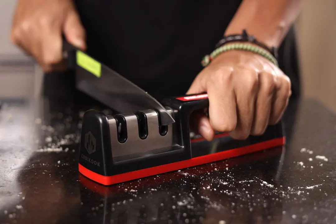 2 hands holding and sharpening a kitchen knife with the Cubikook on a salt-sprinkled countertop