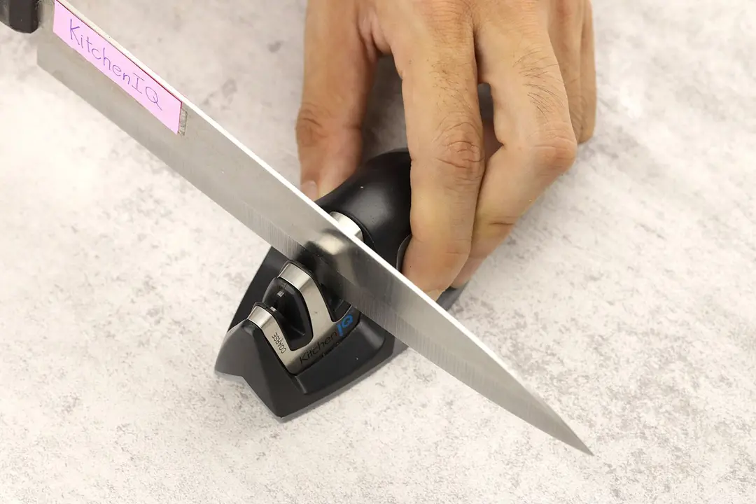 A knife being sharpened with the KitchenIQ, the sharpener being held in one hand