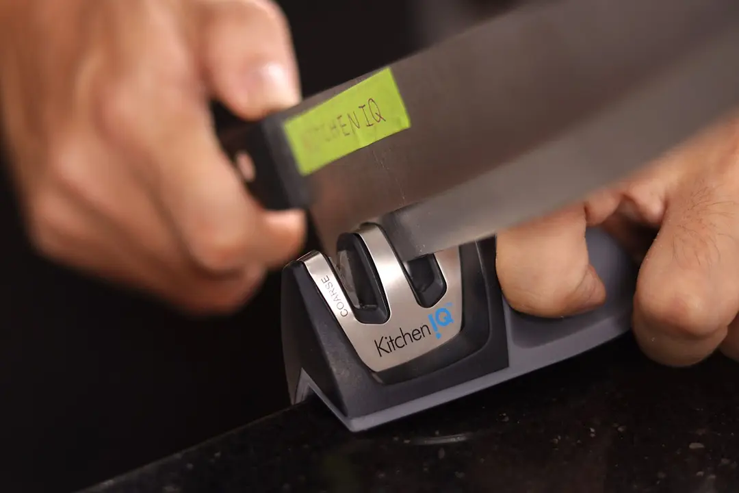 Two hands holding and sharpening a knife with the KitchenIQ on a countertop edge