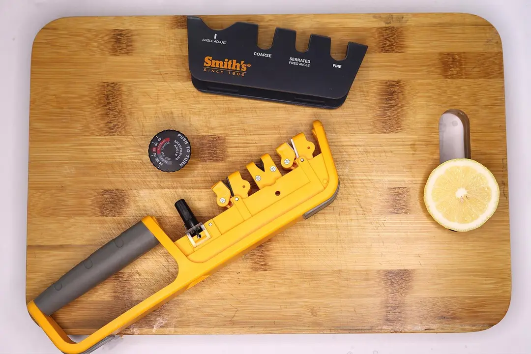 The Smith’s Pull-thru sharpener with cover and angle knob detached on a cutting board, and a lemon slice