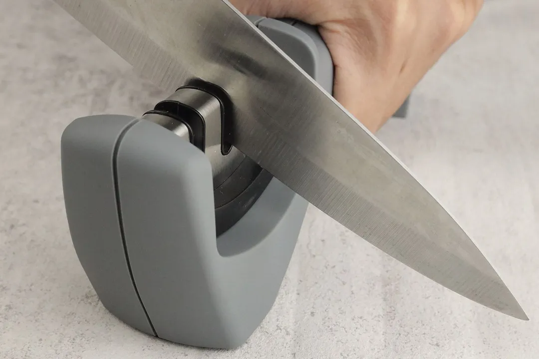 A hand holding the Amesser knife sharpener and sharpening a kitchen knife with it