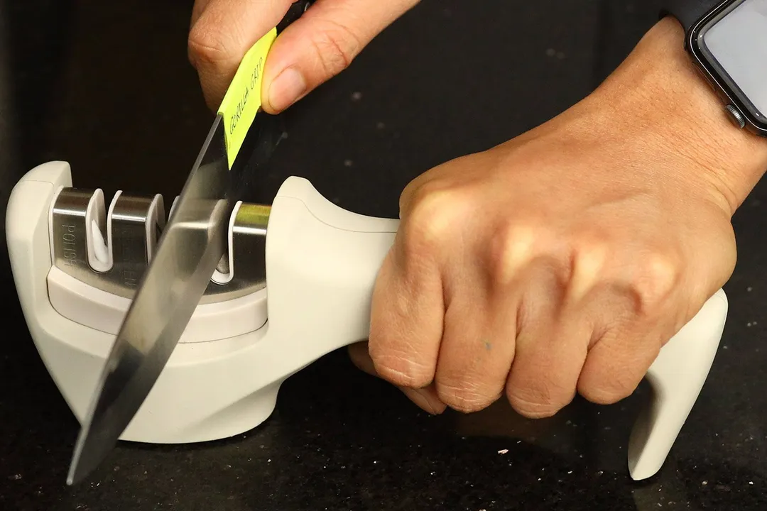 2 hands holding and sharpening a kitchen knife with the Gorilla Grip sharpener on a countertop