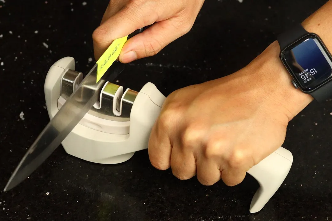 2 hands holding and sharpening a kitchen knife with the Gorilla Grip on a salt-sprinkled countertop
