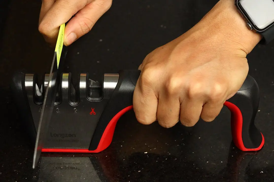 A hand holding the Longzon on a kitchen countertop and sharpening a knife with it.